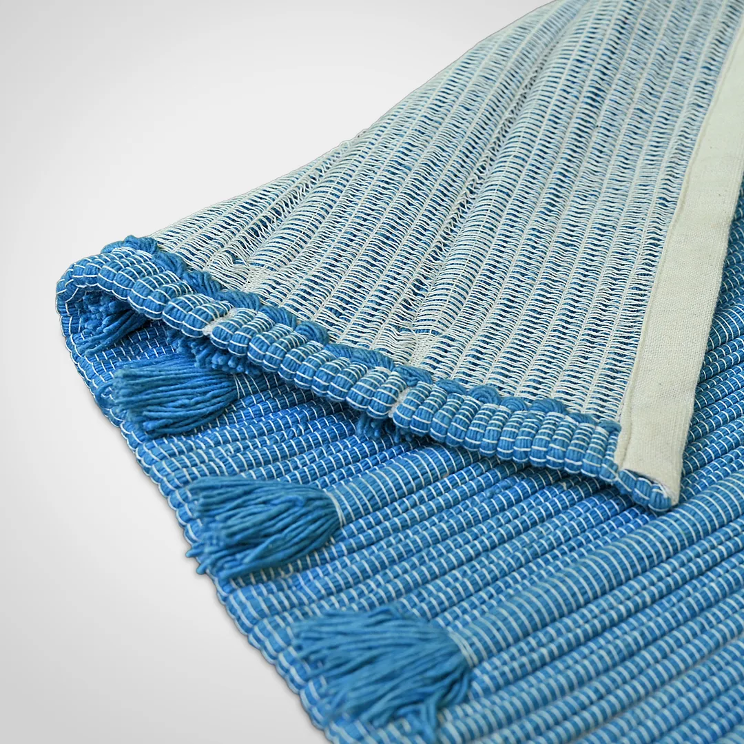 Indico mat with one corner folded back to show its paler underside beside the ribbed indigo weave and hand-knotted tassels
