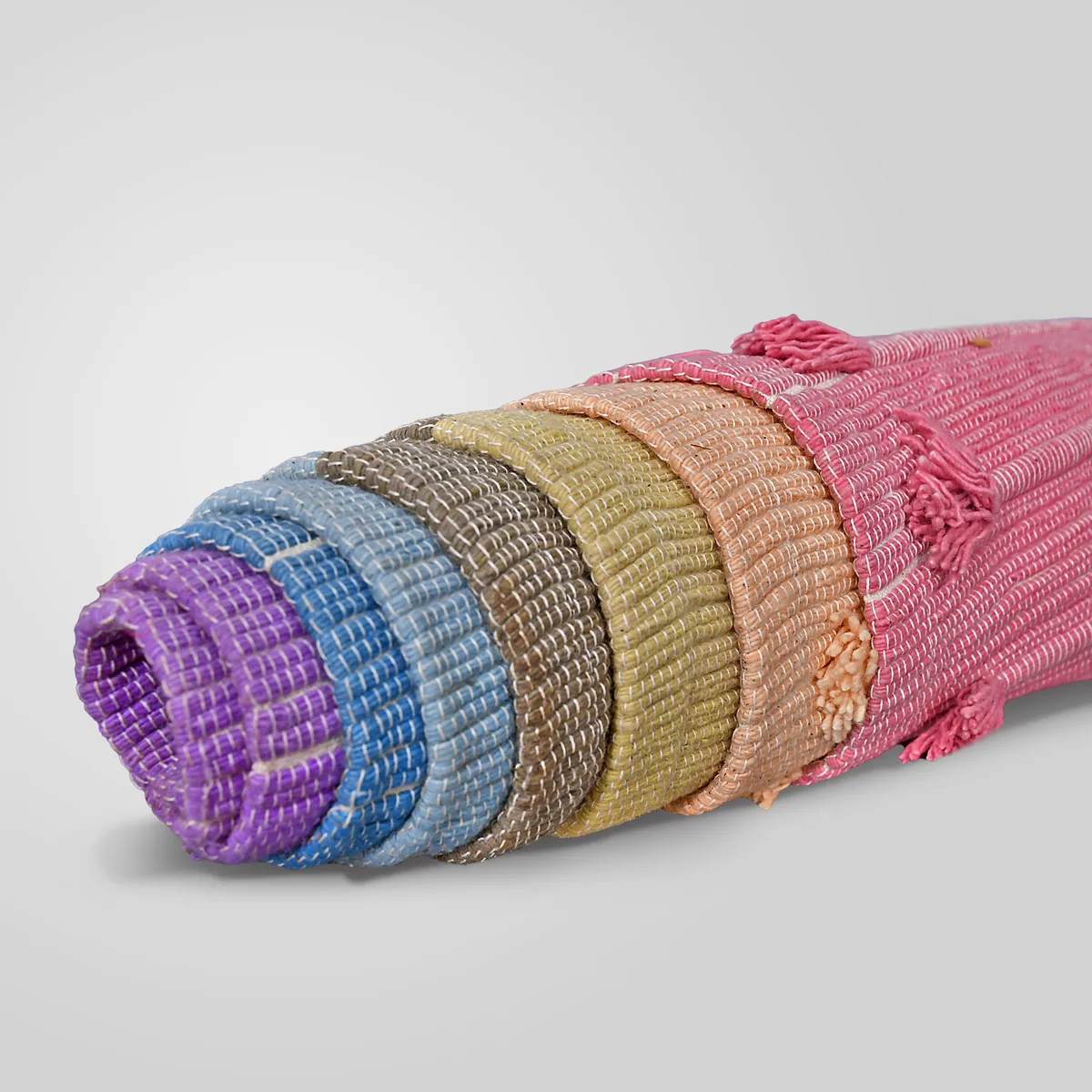 The Prana Shakti rug rolled up, showing its seven plant-dyed colour bands and rose cotton ground